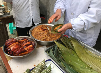 Here is a lady making zongzi. It's grain and a slab of pork wrapped in bamboo leaf. Then it's boiled for awhile and tastes quite good. Fresh made zongzi